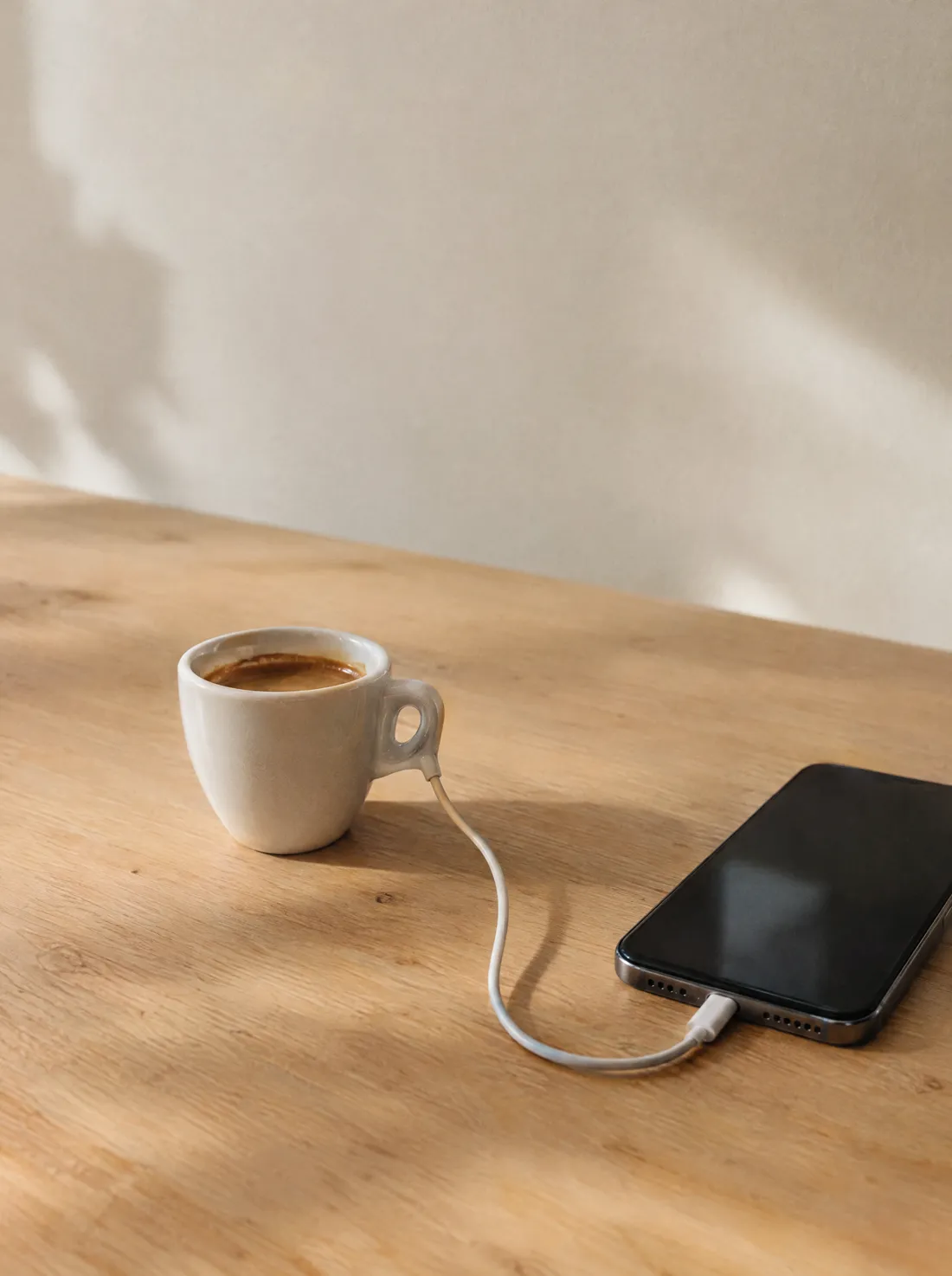 Una tazzina di caffè col cavo di ricarica collegato al telefono